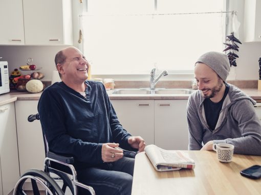 When a friend is hurt and in a temporary wheelchair, it is time to visit and change is mind. Two man having a chat and a coffee in a home kitchen, talking about the morning paper. Horizontal waist up indoors shot in natural light. This was shot in Montreal, Canada.